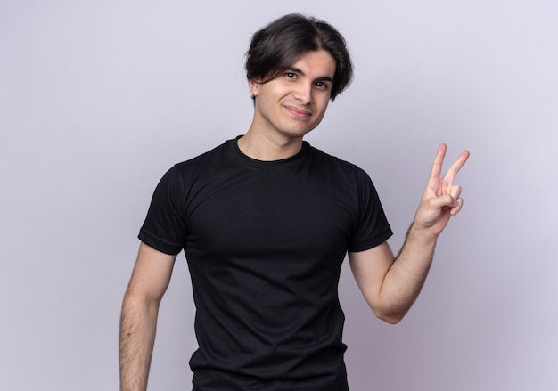 Pleased young handsome guy wearing black t-shirt showing peace gesture isolated on white wall