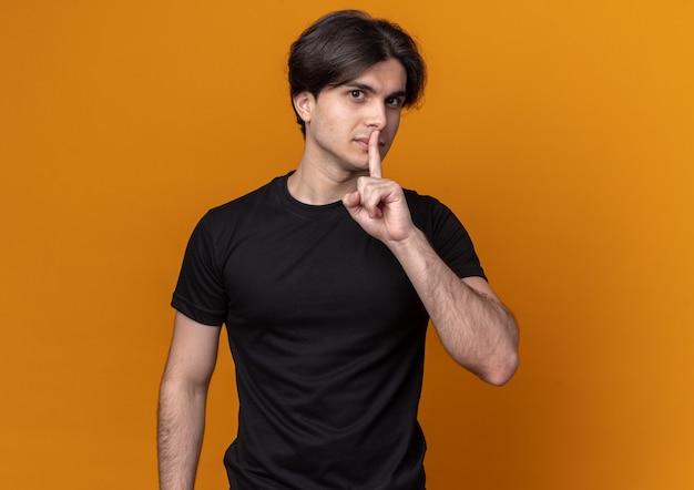 Free photo pleased young handsome guy wearing black t-shirt showing silence gesture isolated on orange wall with copy space