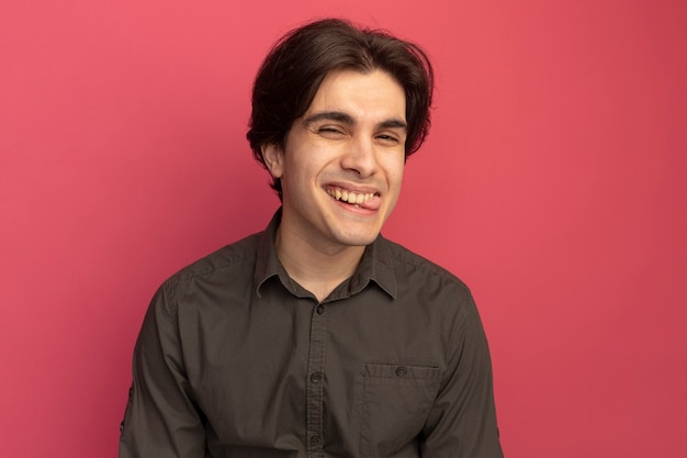 Pleased young handsome guy wearing black t-shirt showing tongue isolated on pink wall