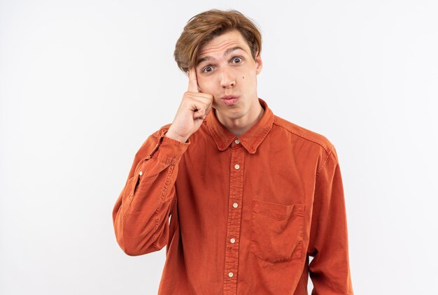 Pleased young handsome guy wearing red shirt putting finger on cheek 