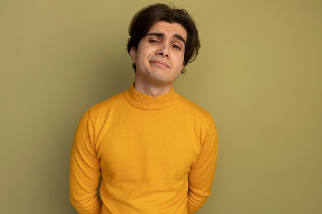 Pleased young handsome guy wearing yellow turtleneck sweater isolated on olive green wall with copy space