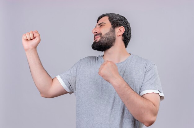 Pleased young handsome man clenching fists with closed eyes isolated on white wall