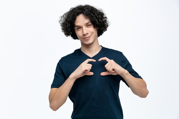 Pleased young handsome man looking at camera making love sign isolated on white background