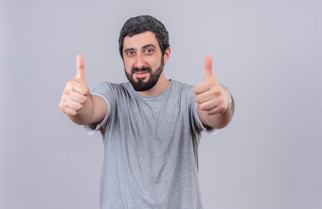 Pleased young handsome man showing thumbs up at front isolated on white wall