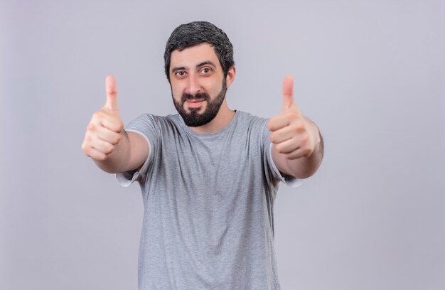 Pleased young handsome man showing thumbs up at front isolated on white wall