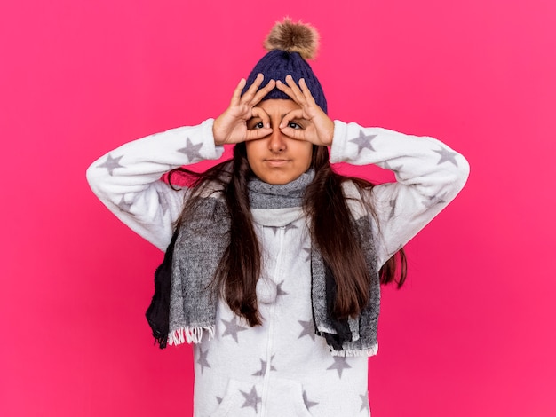 Free photo pleased young ill girl wearing winter hat with scarf showing look gesture isolated on pink background