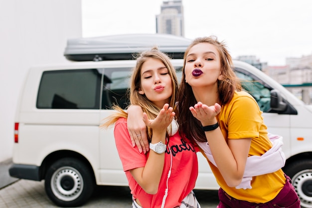 Foto gratuita soddisfatte giovani donne in abito estivo elegante in posa con un'espressione del viso adorabile prima di partire in macchina bianca