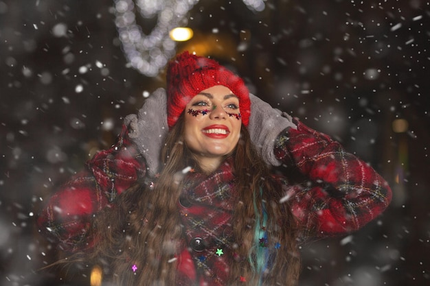クリスマスフェアで雪の天気を楽しんでいる若い長い髪の女性を喜ばせる