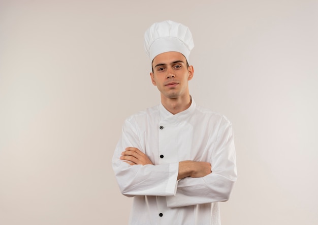 Lieto giovane cuoco maschio che indossa uniformi dello chef incrocio le mani sul muro bianco isolato con spazio di copia