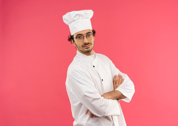 pleased young male cook wearing chef uniform and glasses crossing hands 