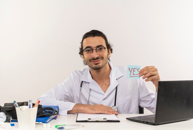 Foto gratuita soddisfatto giovane medico maschio con occhiali medicali che indossa veste medica con stetoscopio