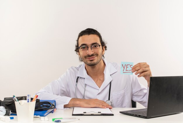 Pleased young male doctor with medical glasses wearing medical robe with stethoscope