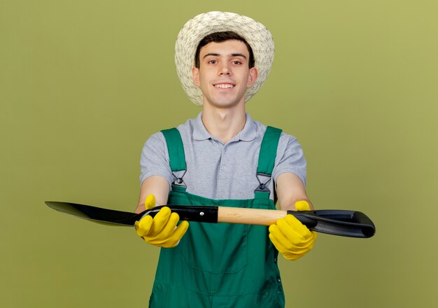 Free photo pleased young male gardener wearing gardening hat holds spade