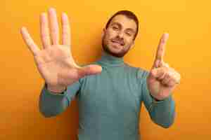 Free photo pleased young man looking at front winking showing six with hands isolated on orange wall