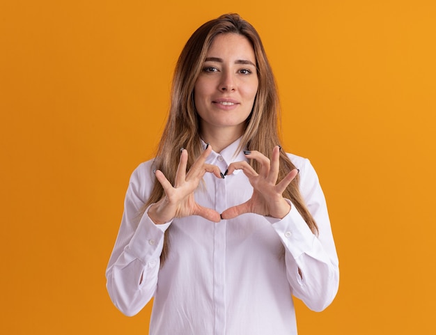 Pleased young pretty caucasian girl gestures heart sign isolated on orange wall with copy space