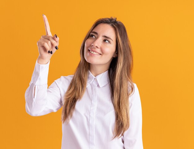 Pleased young pretty caucasian girl looks and points up on orange 