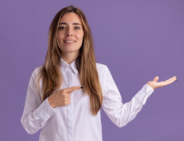 Pleased young pretty caucasian girl points at empty hand on purple 