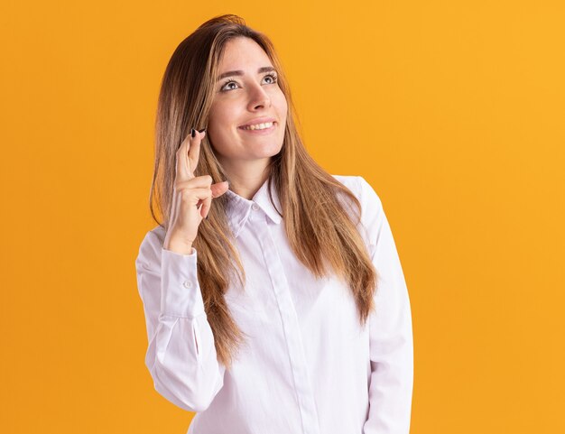 Pleased young pretty caucasian girl stands with crossed fingers looking up