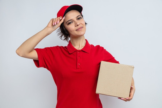 Pleased young pretty delivery woman holding cardboard box