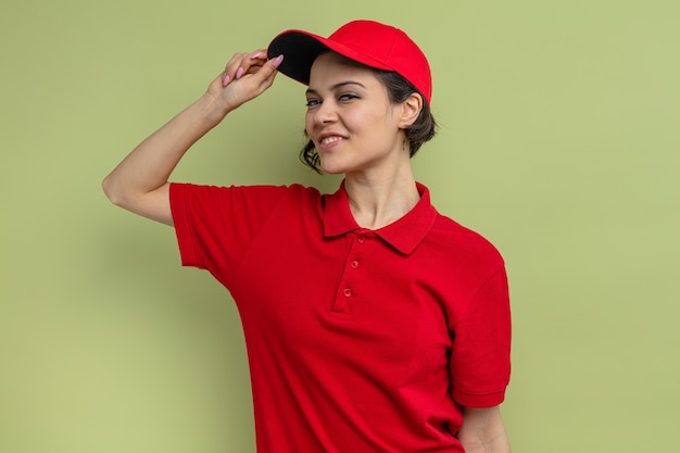 Pleased young pretty delivery woman holding her cap and 