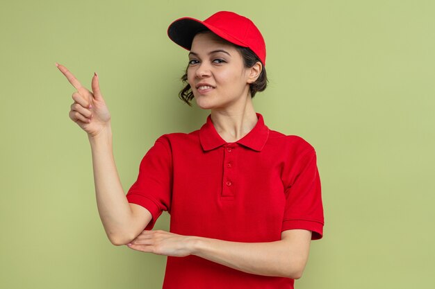 Pleased young pretty delivery woman pointing at side 