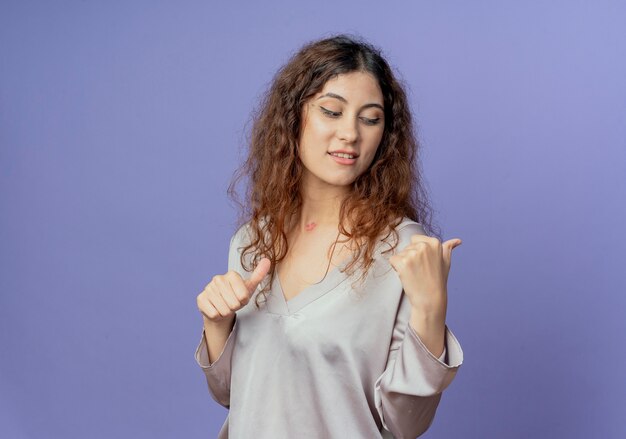 Pleased young pretty girl points at side isolated on blue wall