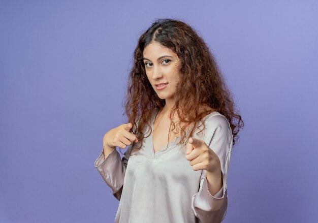 Pleased young pretty girl points you isolated on blue wall