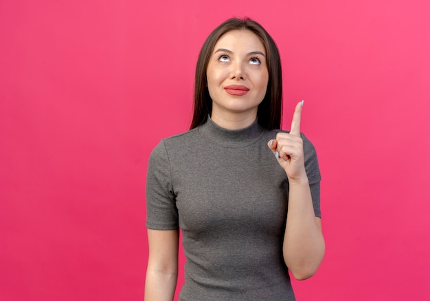 Pleased young pretty woman looking and pointing up isolated on pink background with copy space