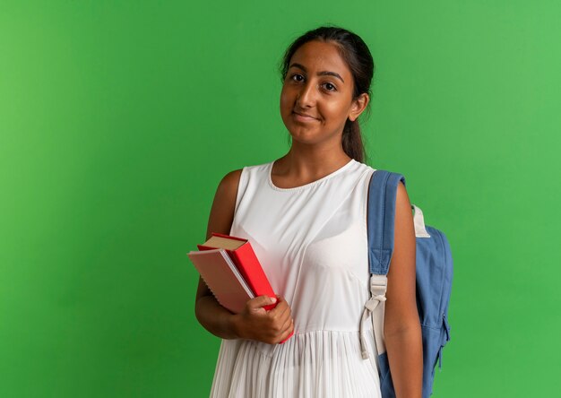 pleased young schoolgirl wearing back bag holding book and notebook