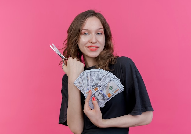 Free photo pleased young slavic female barber wearing uniform holding scissors and money isolated on pink background with copy space