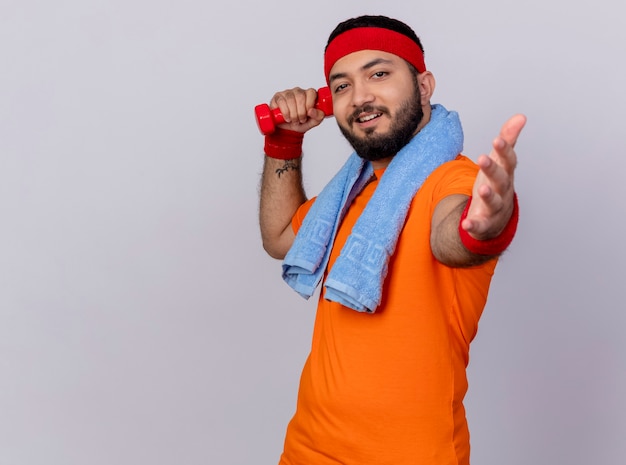 Free photo pleased young sporty man wearing headband and wristband holding dumbbell with towel on shoulder