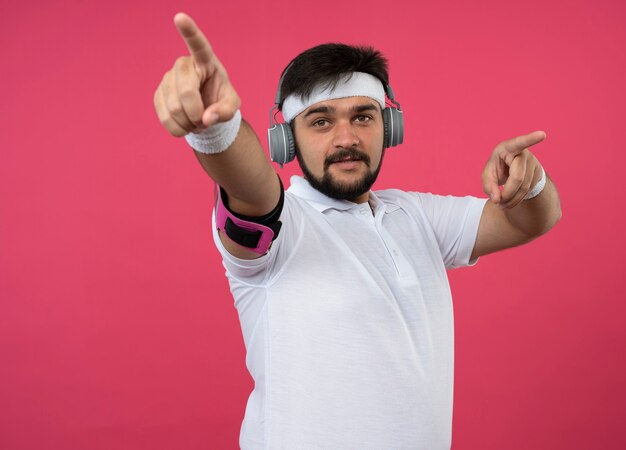 ヘッドバンドとリストバンドを身に着けている若いスポーティな男性を喜ばせ、ヘッドフォンと電話の腕章を前面に向けます