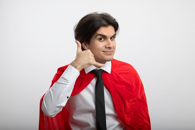 Pleased young superhero guy looking at camera wearing tie showing phone call gesture isolated on white