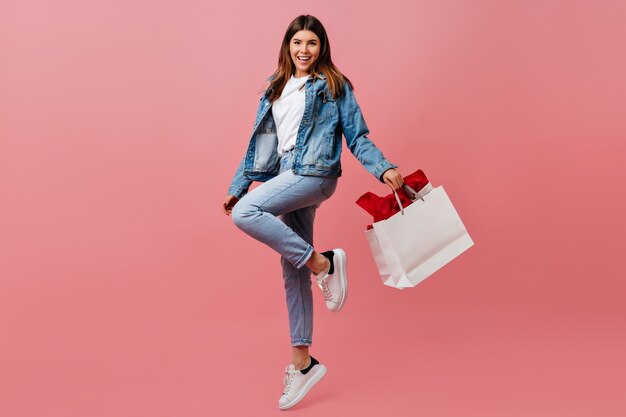 Довольная молодая женщина, держащая сумку магазина. Очаровательная европейская девушка в джинсовой одежде в полный рост.