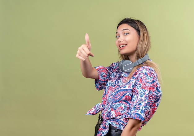 Una giovane donna soddisfatta che indossa la camicia stampata paisley in cuffie che mostra i pollici in su