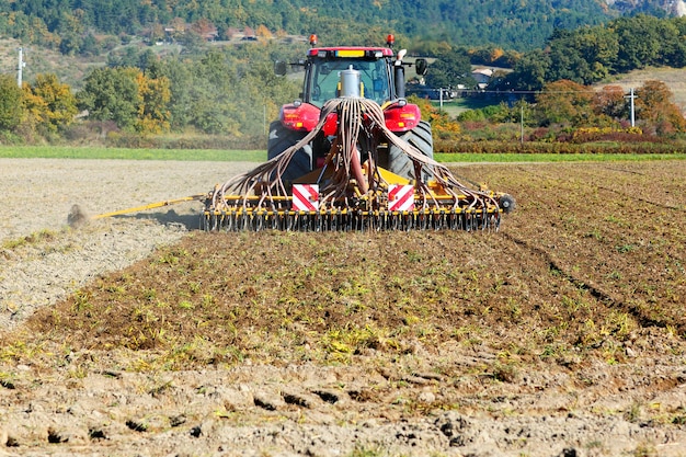 Пахота тяжелого трактора во время культивации сельскохозяйственных работ на поле с плугом