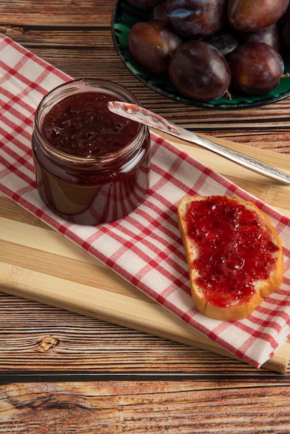 Plum confiture in the glass jar and on the toast on the checked kitchen towel.