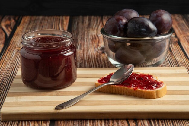 Plum confiture in a glass jar with toast breads and fruits.