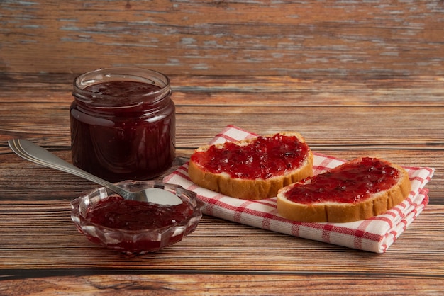 Plum confiture in a glass jar with toast breads on a kitchen towel.