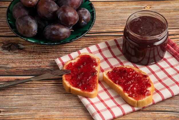 Plum confiture on toast breads and fruits on a checked towel.
