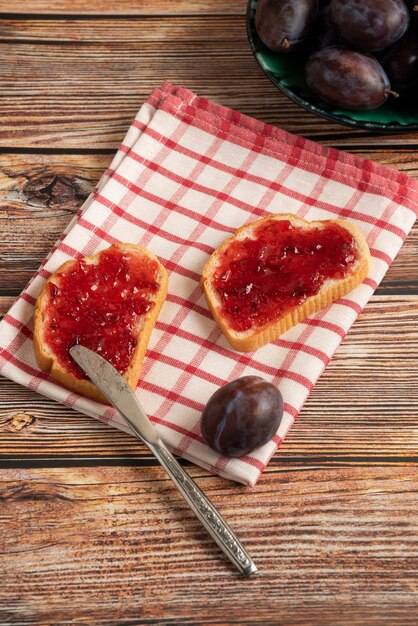 Plum confiture on toast breads and fruits on a checked towel.