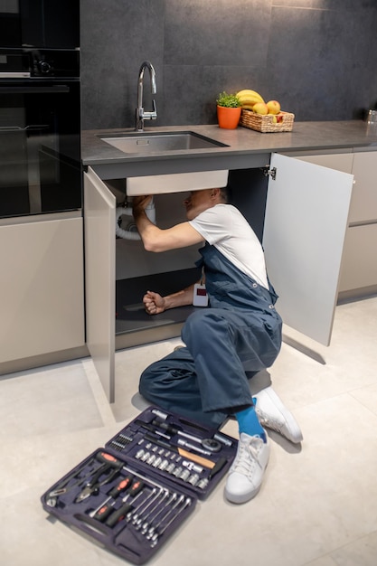 Plumbing inspection Man in overalls with badge reclining on floor with tools