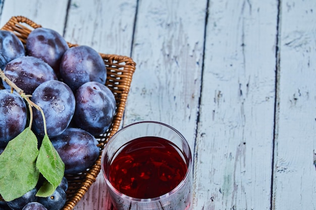 Plums on basket on blue with a glass of juice.