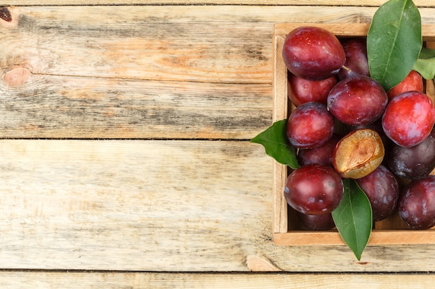 Plums in a wooden crate on a wooden board background. top view. free space for your text