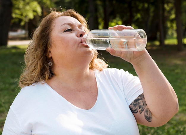 プラスサイズの女性が公園で水を飲む