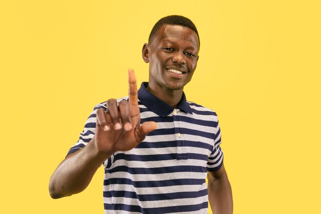 Point at you. Young african-american man isolated on yellow studio background, facial expression. Beautiful male half-lenght portrait. Concept of human emotions, facial expression.