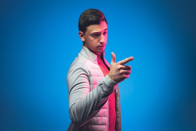 Указывая, выбирая. Портрет кавказского человека, изолированные на синей стене в розовом неоновом свете. Красивая мужская модель в повседневной одежде. Понятие о человеческих эмоциях, выражение лица Copyspace.