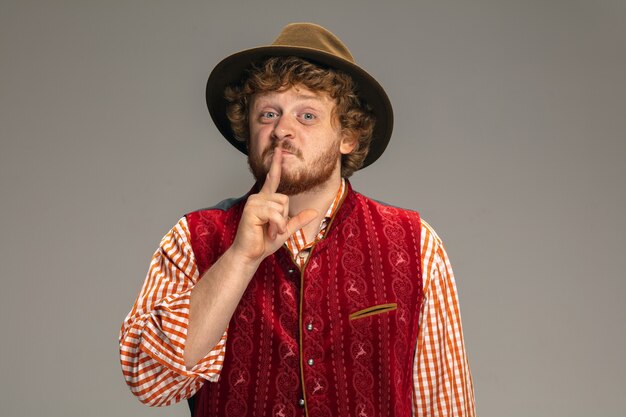 Pointing. Happy smiling man dressed in traditional Austrian or Bavarian costume gesturing isolated on grey studio