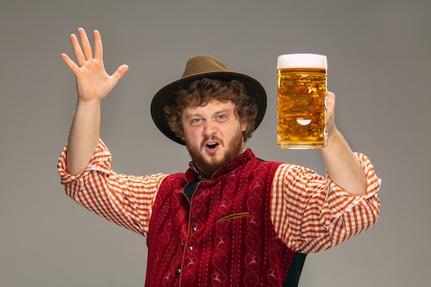 Pointing. Happy smiling man dressed in traditional Austrian or Bavarian costume gesturing isolated on grey studio