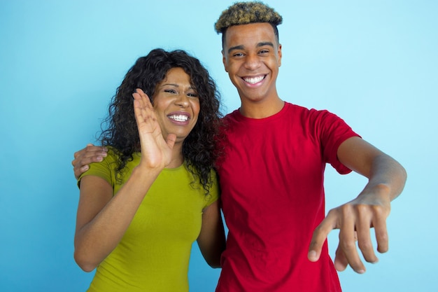 Указывая, смеясь. Молодой эмоциональный афро-американский мужчина и женщина в красочной одежде на синем фоне. Прекрасная пара. Понятие человеческих эмоций, выражения лица, отношений, рекламы, дружбы.
